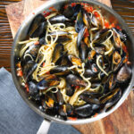 Mussel linguine in a butter and white wine sauce with garlic, chilli and tomatoes in a pan.