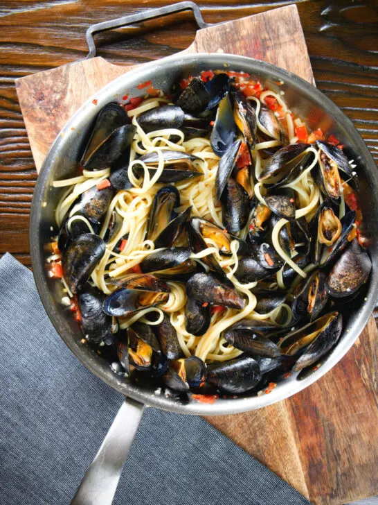 Mussel linguine in a butter and white wine sauce with garlic, chilli and tomatoes in a pan.