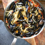 Mussel linguine in a butter and white wine sauce with garlic, chilli and tomatoes in a pan.