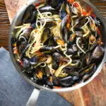Mussel linguine in a butter and white wine sauce with garlic, chilli and tomatoes in a pan.