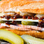 Close-up ploughman's lunch sandwich with ham cheese and pickles on a crusty baguette.