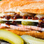 Close-up ploughman's lunch sandwich with ham cheese and pickles on a crusty baguette.