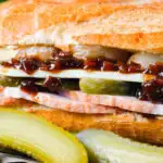 Close-up ploughman's lunch sandwich with ham cheese and pickles on a crusty baguette.