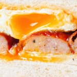 Close-up sausage and fried egg breakfast sandwich on thick sliced white bread.