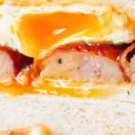 Close-up sausage and fried egg breakfast sandwich on thick sliced white bread.