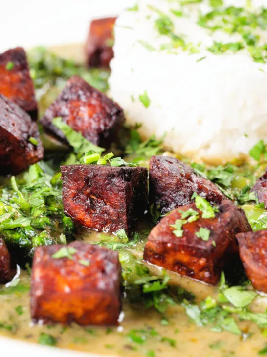 Close-up crispy tofu Thai green curry with fresh herbs and jasmine rice.