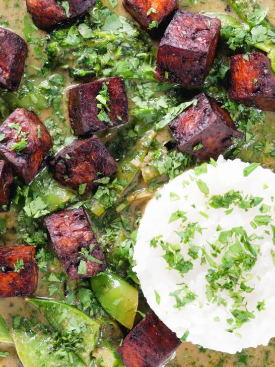 Overhead close-up crispy tofu Thai green curry with fresh herbs and jasmine rice.