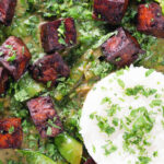 Overhead close-up crispy tofu Thai green curry with fresh herbs and jasmine rice.