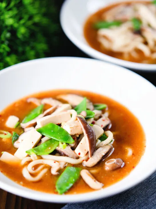 Two bowls of vegan miso noodle soup with tofu, mangetout and shiitake mushrooms.
