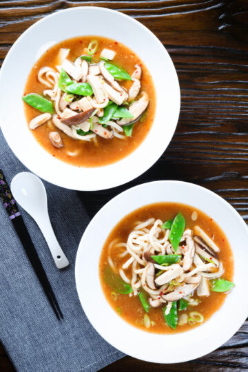 Two bowls (overhead) of vegan miso noodle soup with tofu, mangetout and shiitake mushrooms.