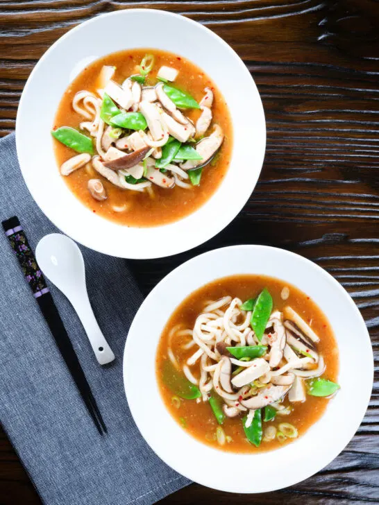 Two bowls (overhead) of vegan miso noodle soup with tofu, mangetout and shiitake mushrooms.