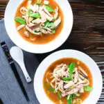 Two bowls (overhead) of vegan miso noodle soup with tofu, mangetout and shiitake mushrooms.