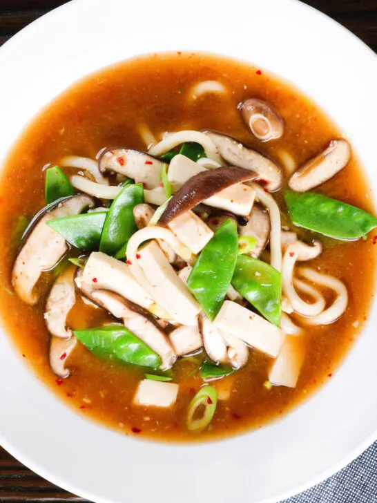 Overhead close-up vegan miso noodle soup with tofu, mangetout and shiitake mushrooms.