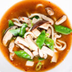 Overhead close-up vegan miso noodle soup with tofu, mangetout and shiitake mushrooms.