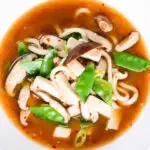 Overhead close-up vegan miso noodle soup with tofu, mangetout and shiitake mushrooms.