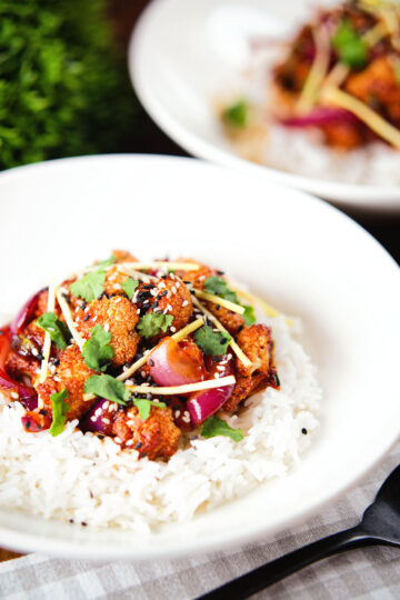 Spicy fried bang bang cauliflower garnished with ginger and coriander served with white rice.