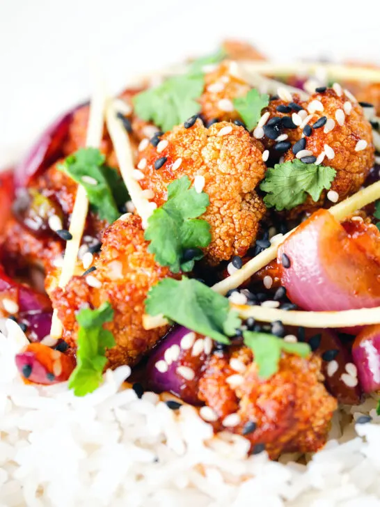Close-up bang bang cauliflower garnished with ginger and coriander served with white rice.
