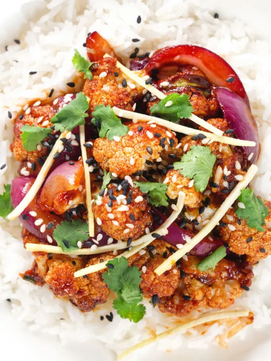 Close-up overhead bang bang cauliflower garnished with ginger and coriander served with white rice.