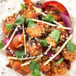 Close-up overhead bang bang cauliflower garnished with ginger and coriander served with white rice.