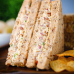 Close-up cheese and onion sandwich with Branston pickle on malted bread served with crisps.