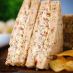 Close-up cheese and onion sandwich with Branston pickle on malted bread served with crisps.