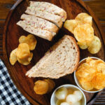 Overhead cheese and onion sandwich with Branston pickle on malted bread served with crisps and pickled onions.
