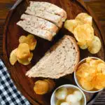 Overhead cheese and onion sandwich with Branston pickle on malted bread served with crisps and pickled onions.