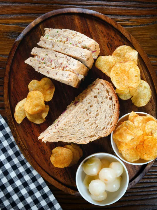Overhead cheese and onion sandwich with Branston pickle on malted bread served with crisps and pickled onions.