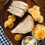 Overhead cheese and onion sandwich with Branston pickle on malted bread served with crisps and pickled onions.