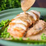 Creamy mustard and cider sauce being poured over a sliced chicken breast.