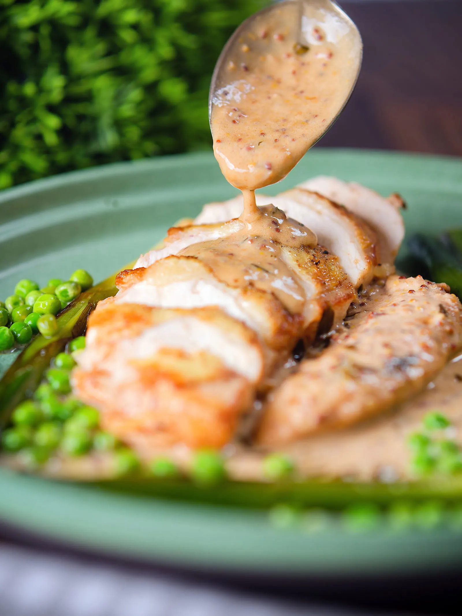 Creamy mustard and cider sauce being poured over a sliced chicken breast.