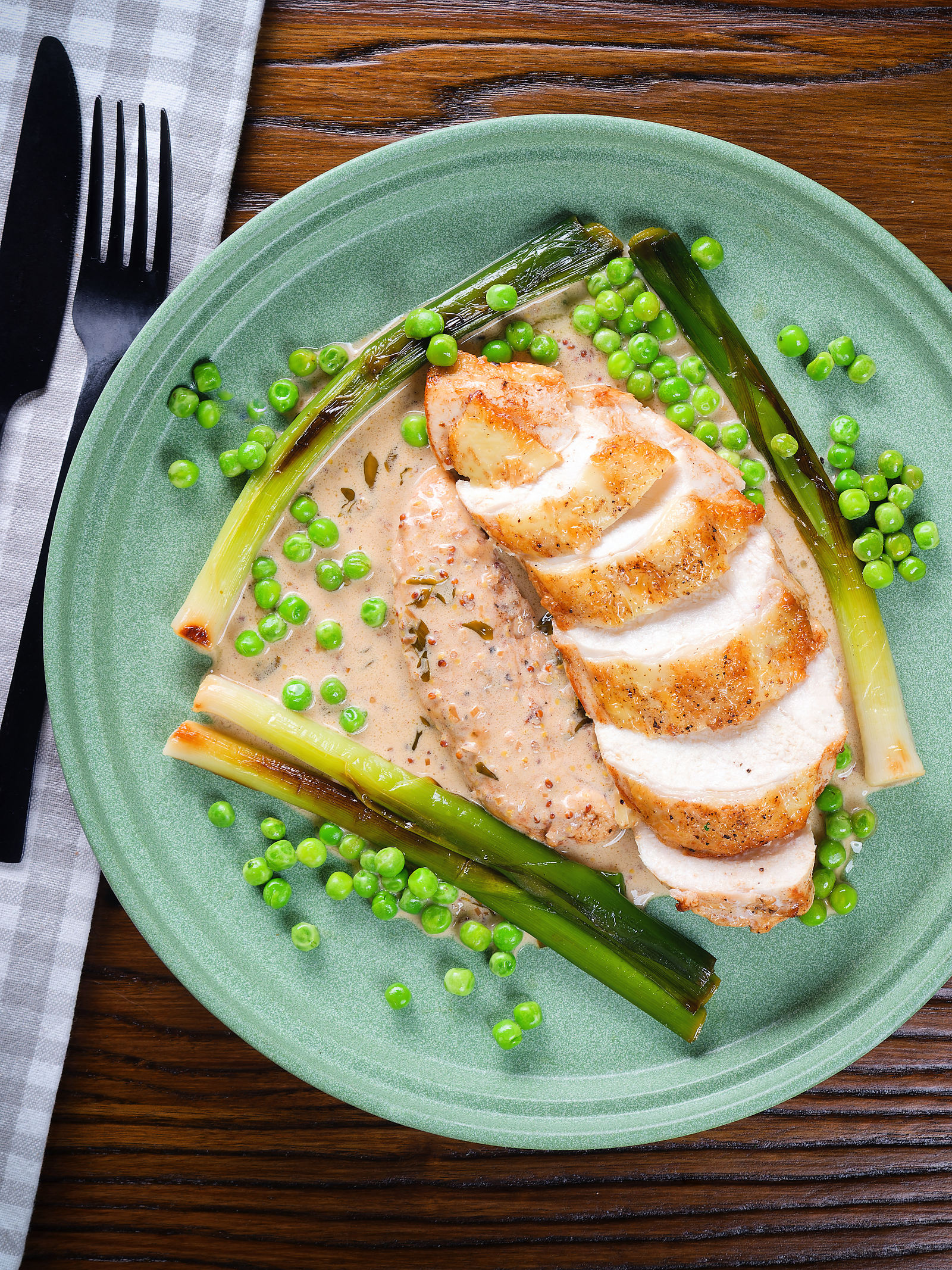Overhead chicken breast in a creamy cider mustard sauce served with baby leeks and peas.