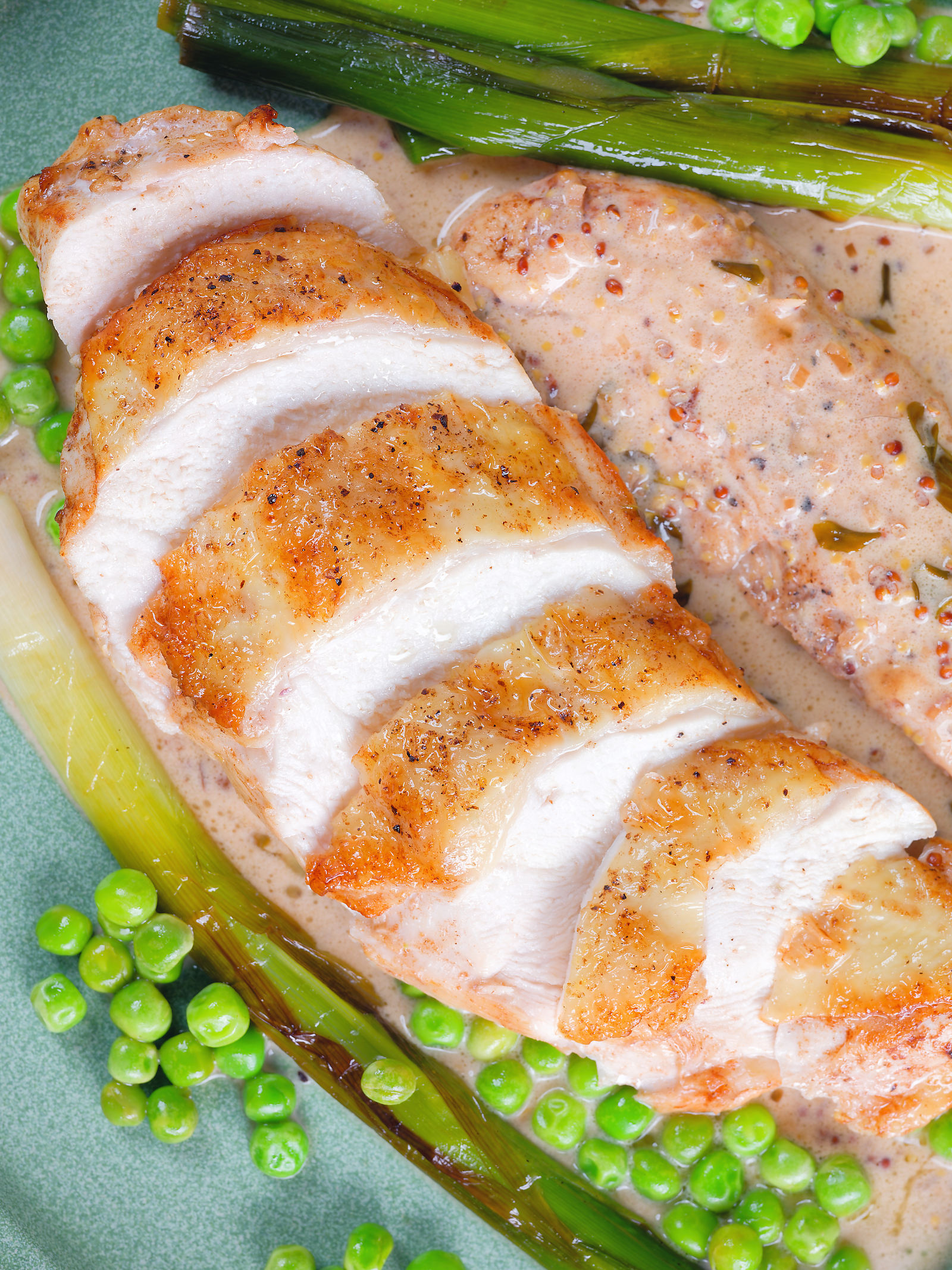 Overhead close-up chicken breast in a creamy cider mustard sauce served with baby leeks and peas.