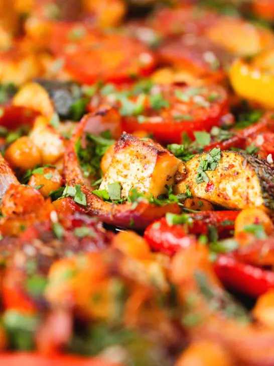 Close-up halloumi tray bake with Mediterranean vegetables, chickpeas and spicy harissa.