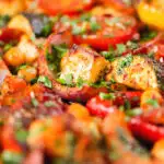 Close-up halloumi tray bake with Mediterranean vegetables, chickpeas and spicy harissa.