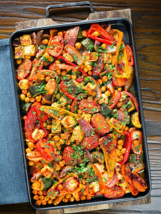 Overhead halloumi tray bake with Mediterranean vegetables, chickpeas and spicy harissa.