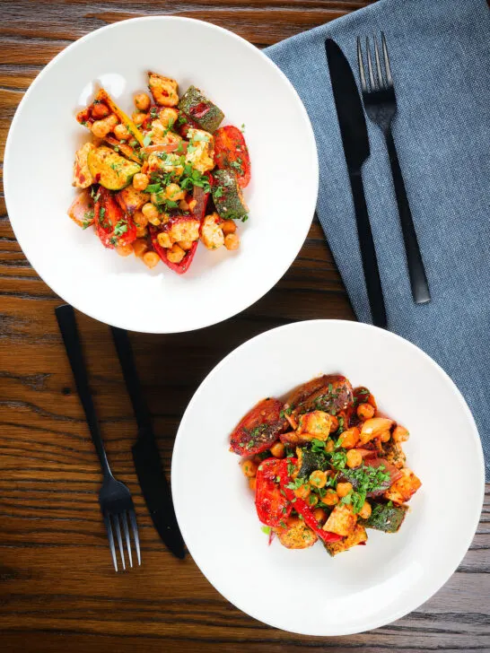 Halloumi cheese tray bake with Mediterranean vegetables, chickpeas and spicy harissa served in two bowls.
