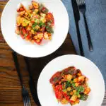 Halloumi cheese tray bake with Mediterranean vegetables, chickpeas and spicy harissa served in two bowls.