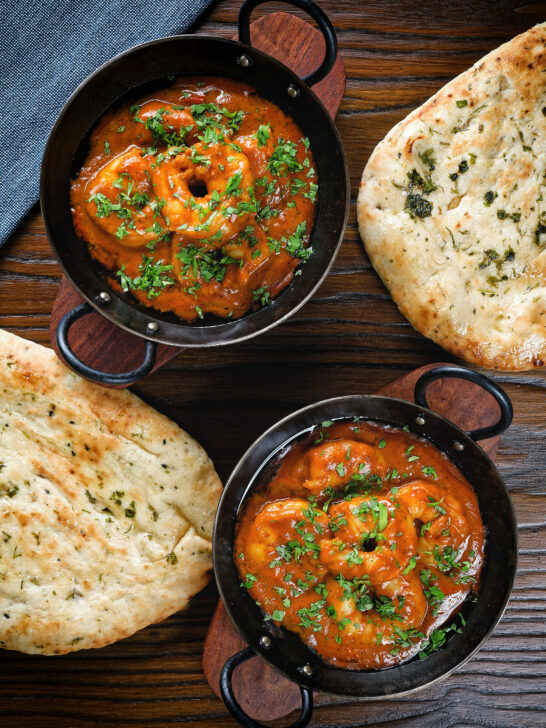 Overhead Indian takeaway inspired king prawn Balti curry with naan bread.