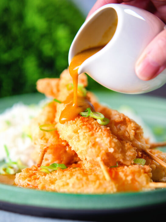 Homemade Japanese curry sauce being poured over king prawn katsu.