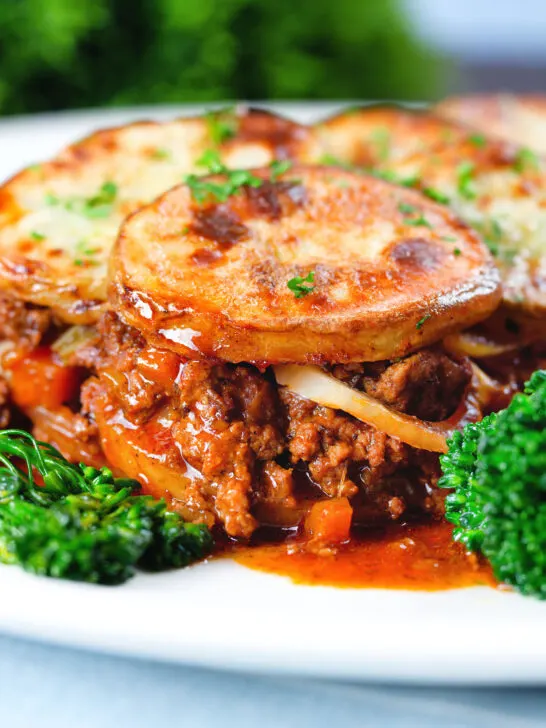 Close-up minced beef and onion hotpot with scalloped potatoes served on a plate with green veggies.