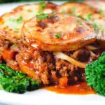 Close-up minced beef and onion hotpot with scalloped potatoes served on a plate with green veggies.
