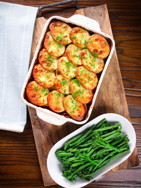 Overhead minced beef and potato hotpot served in a baking dish with broccoli and green beans.