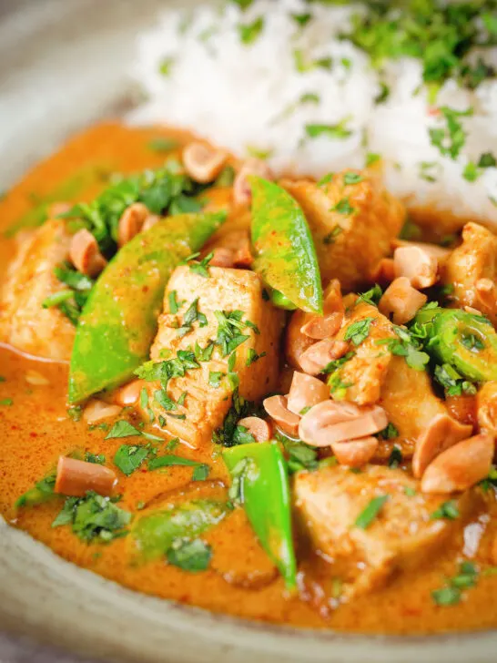 Close-up satay chicken curry with peanuts and coriander served with steamed rice.