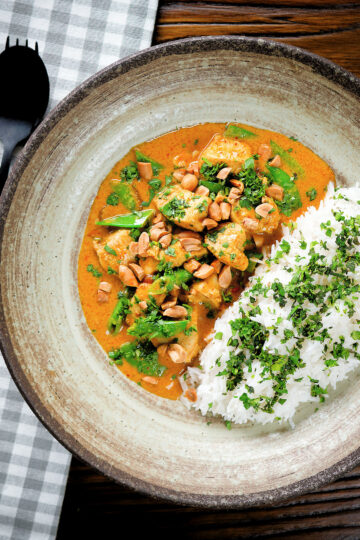 Overhead satay chicken curry with peanuts and coriander served with steamed rice.