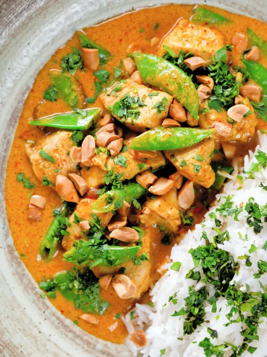 Overhead close-up satay chicken curry with peanuts and coriander served with steamed rice.