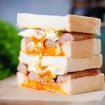 Close-up sausage and fried egg breakfast sandwich with a runny yolk served with coffee.