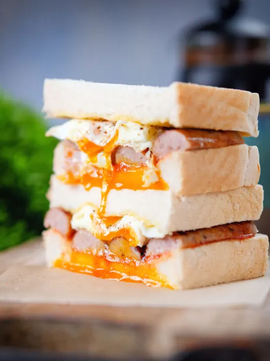 Close-up sausage and fried egg breakfast sandwich with a runny yolk served with coffee.