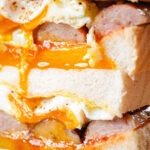 Close-up sausage and fried egg breakfast sandwich with a runny yolk.