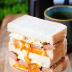 Simple sausage and fried egg breakfast sandwich with a runny yolk served with coffee.